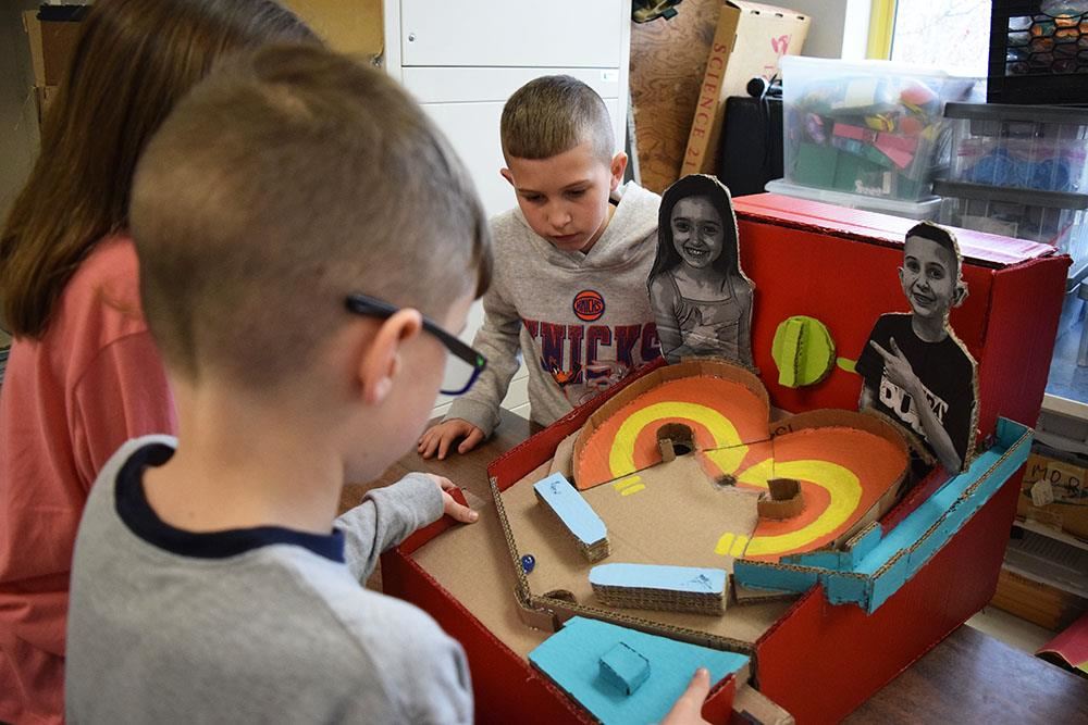 student plays a game while its maker looks on